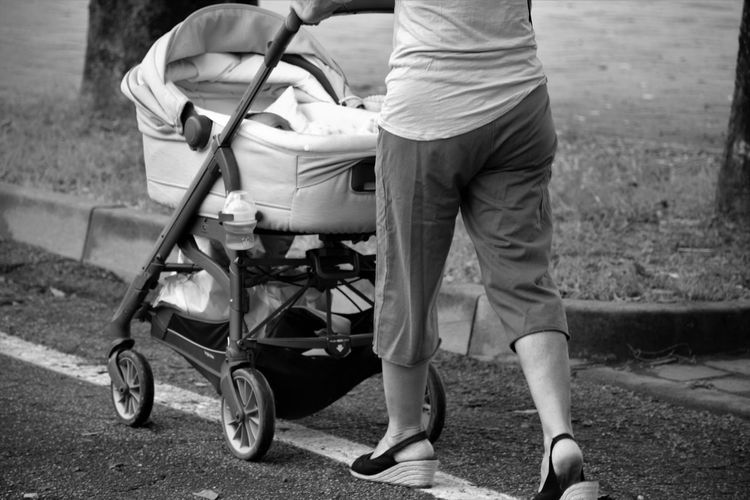 Low section of woman walking with pram on road