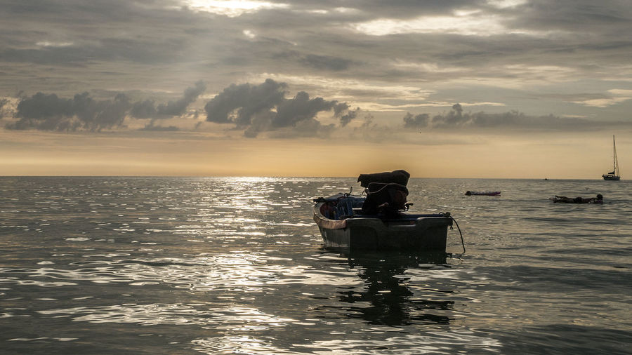 Motorboat moored on sea against cloudy sky during sunset