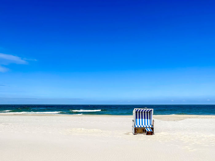 Deck chair on beach against blue sky