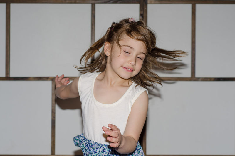 Excited girl with tousled hair jumping against wall at home