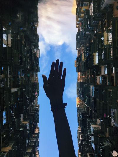 Low angle view of hand against sky in city