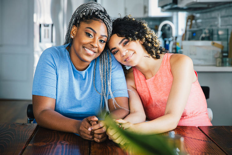 Portrait of confident happy lesbians sitting at table in kitchen