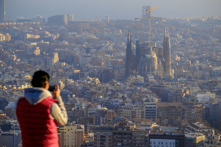 Rear view of man photographing sagrada familia amidst city