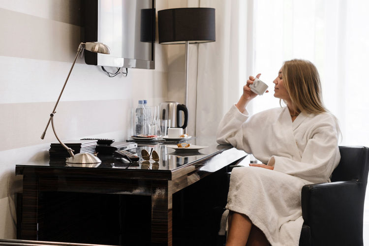 Woman wearing bathrobe in hotel room. person in 20s in bedroom. enjoying morning 