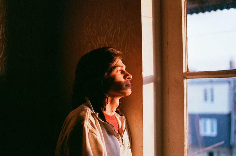 Portrait of young woman looking away while standing against window