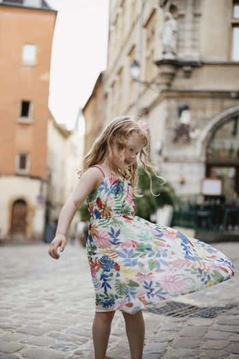 Happy cute girl spinning on street against buildings in city
