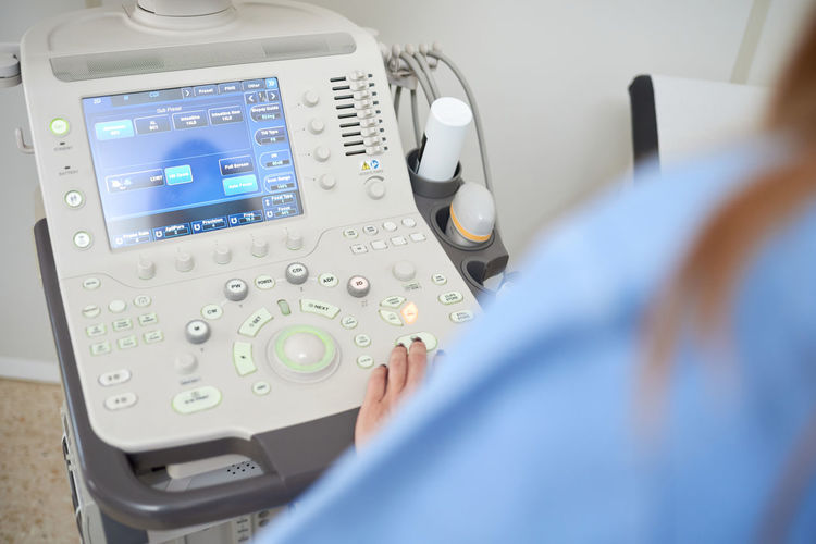 From above back view of crop unrecognizable ultrasound technician using scanner during sonography diagnostic