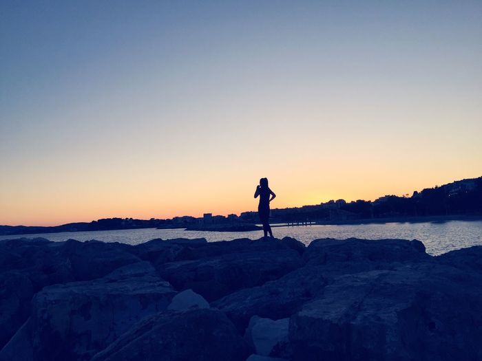 Silhouette woman standing on rock at beach against sunset clear sky