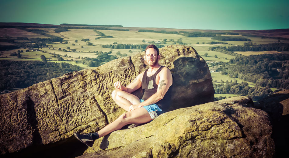 Portrait of man sitting on rock against sky