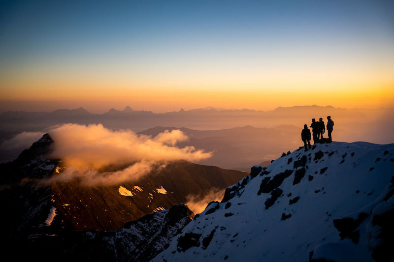 Silhouette people on snowcapped mountain against sky during sunrise