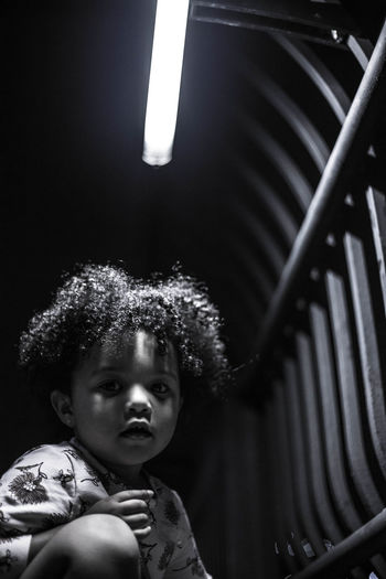 Portrait of kid with curly hair sitting in illuminated room