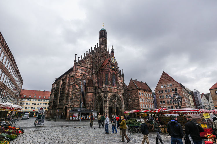 People walking on street by frauenkirche against cloudy sky