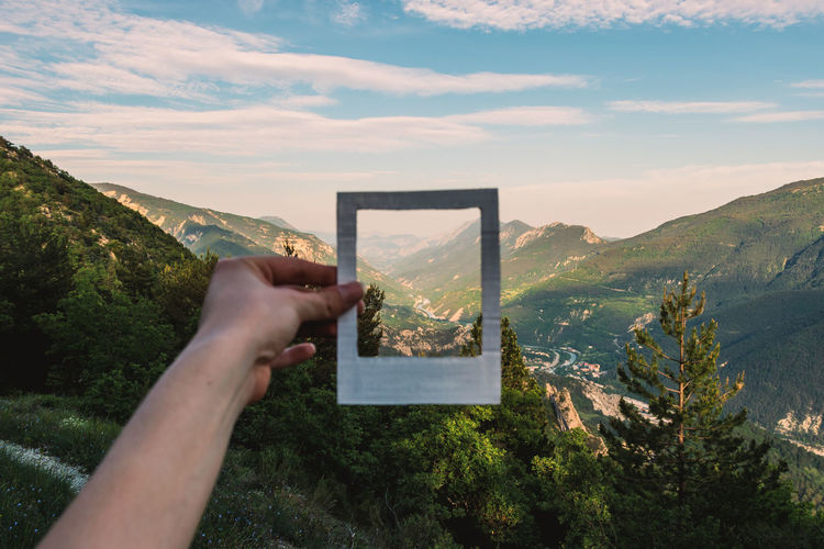 Cropped hand of woman holding picture frame against landscape