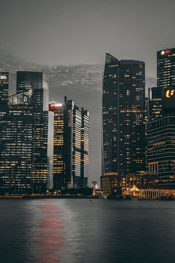 Illuminated buildings by sea against sky at night