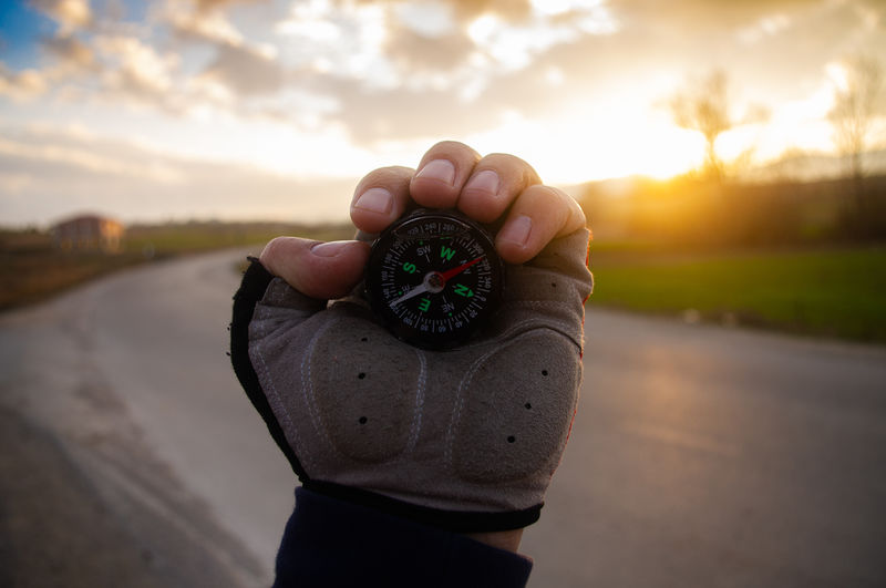 Midsection of man holding umbrella while standing on road during sunset