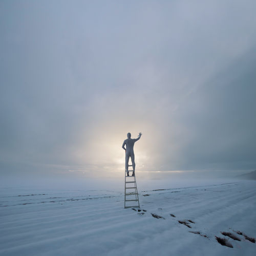 Digital composite image of man standing on ladder at snowcapped landscape against sky during sunset