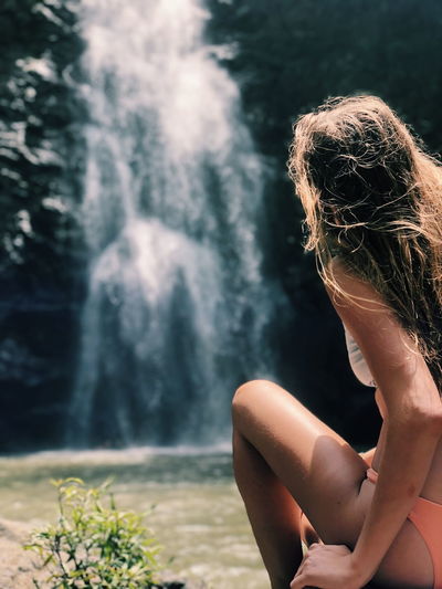 Woman sitting against waterfall in forest