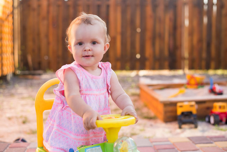 Portrait of cute baby girl sitting on toy car in yard