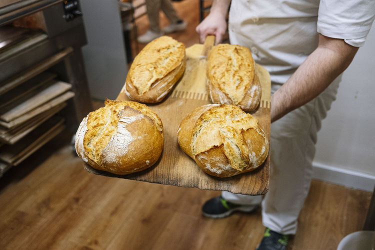Male chef holding baked bread on pizza peel in commercial kitchen at bakery