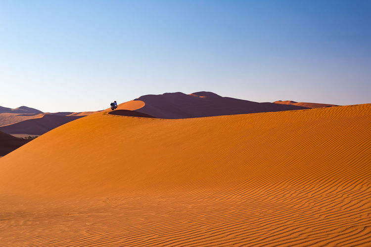 Rear view of woman crouching on desert against sky