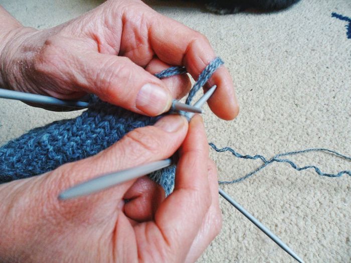 Cropped hands of woman knitting wool at home