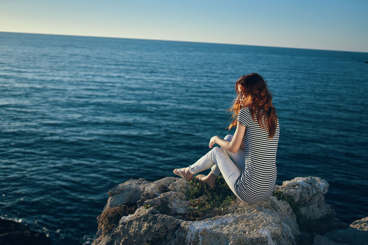 Woman sitting on rock looking at sea