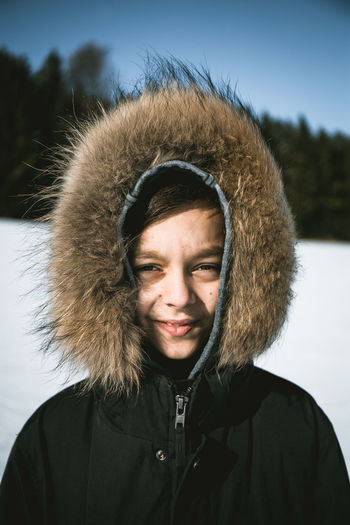 Portrait of smiling boy standing on snow field against sky
