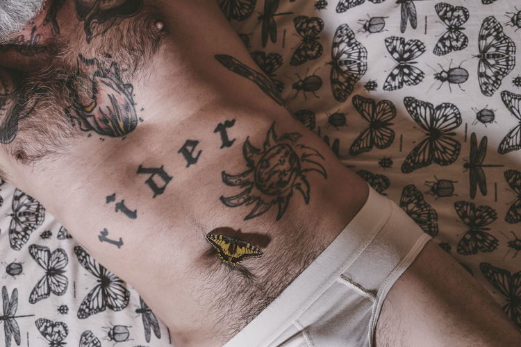 High angle view of a body parte of man with tattoos lying on the bed with a butterfly