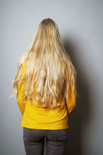 Rear view of woman standing against yellow background