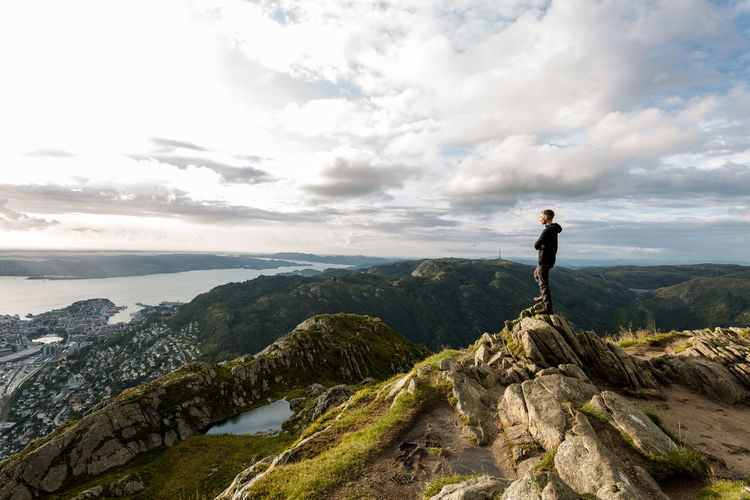 Man standing on rock looking at mountain against sky
