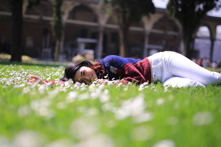Portrait of smiling woman lying on grassy field during sunny day