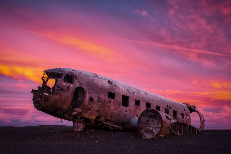 Abandoned airplane on beach against sky during sunset