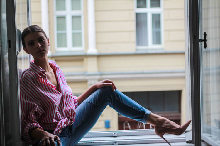 Full length of woman sitting on window of building