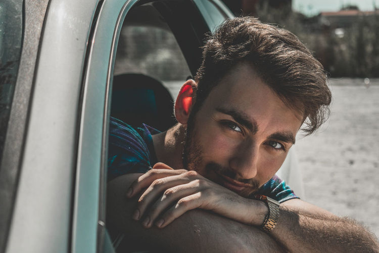 Portrait of young man sitting by car window