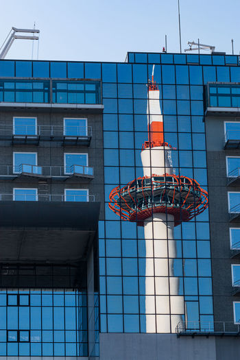 Full frame reflected view of a modern tower against a glass mirrored building against clear blue sky