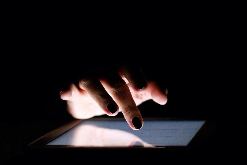 Cropped image of female hand touching digital tablet over black background