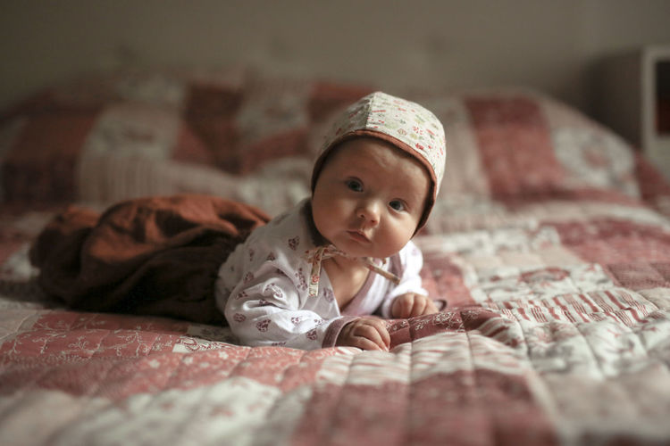 Baby in bonnet lies on the bedspread in the bedroom, 4 months. real interior and natural fabrics