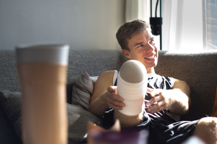 Midsection of man putting on prosthetic limb while sitting on sofa at home