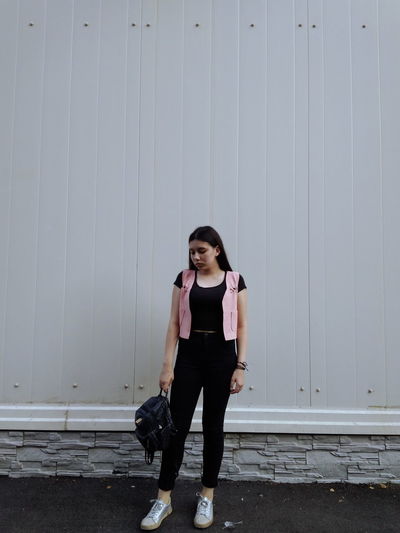 Full length of young woman with backpack standing against wall