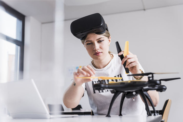 Young woman with laptop and vr glasses at desk examining drone