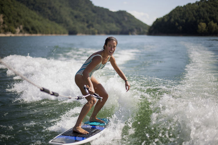 Girl surfing in lake against mountains