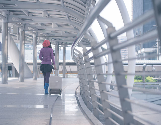 Rear view of woman walking with luggage on footbridge in city