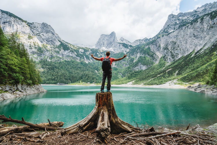Happy traveler standing on tree stump admiring dachstein peak mountains on upper gosau lake, austria