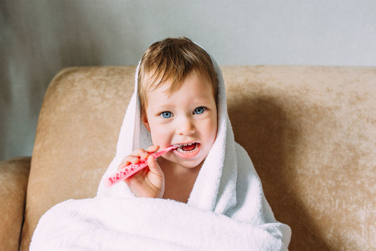 Portrait of cute baby brushing teeth while sitting on sofa