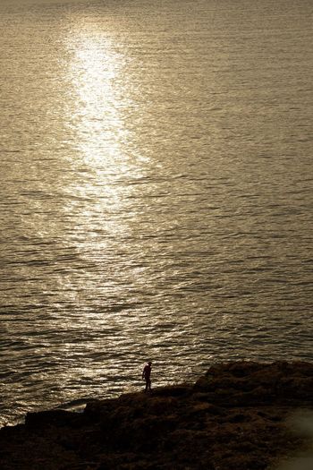 Silhouette person standing on beach against sea during sunrise