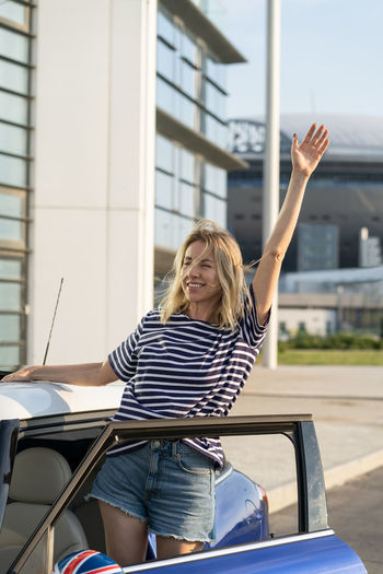Carefree female driver look out of car wave hand happy to go on road trip. woman outside new vehicle
