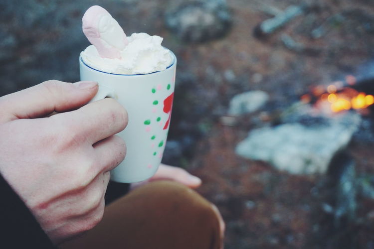 Cropped image of man holding hot chocolate by campfire in forest