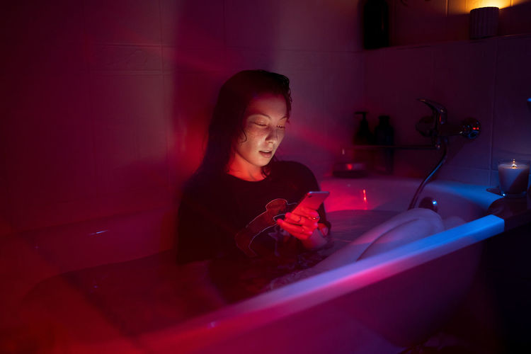 Unhappy girl addicted from social media and following ex-boyfriend sit in dark bath in wet clothes