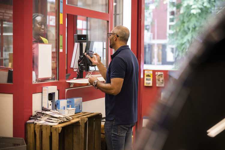 Mature man paying through mobile payment while standing at checkout counter in hardware store