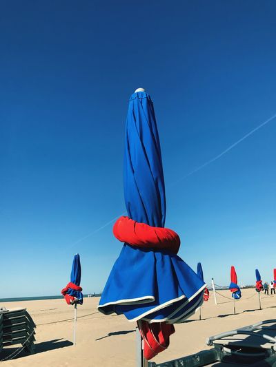 Low angle view of umbrellas on beach against clear blue sky